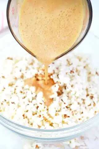 pouring caramel mixture over popcorn in a bowl
