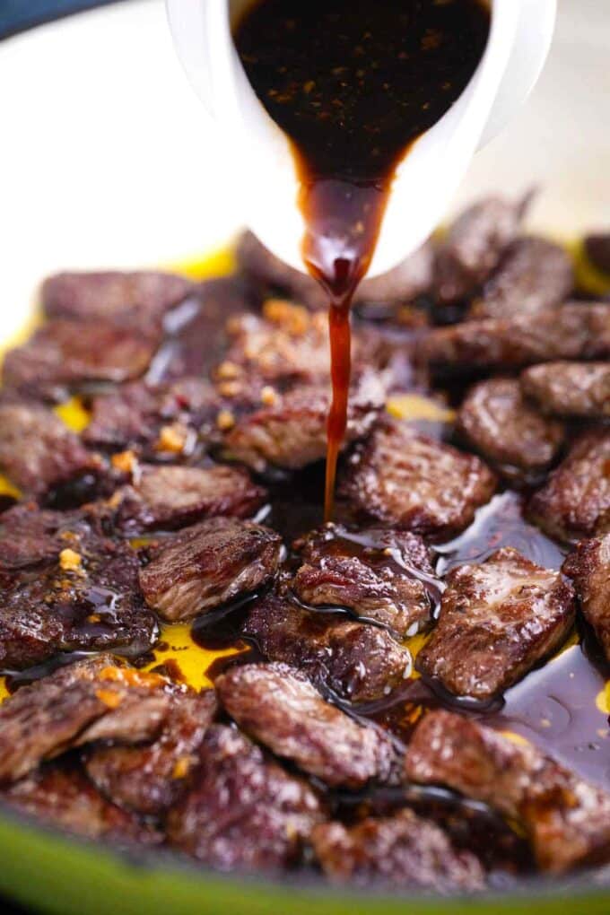 adding honey garlic sauce to steak pieces in a skillet