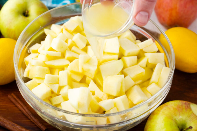 Drizzling lemon juice over chopped apples in a bowl.