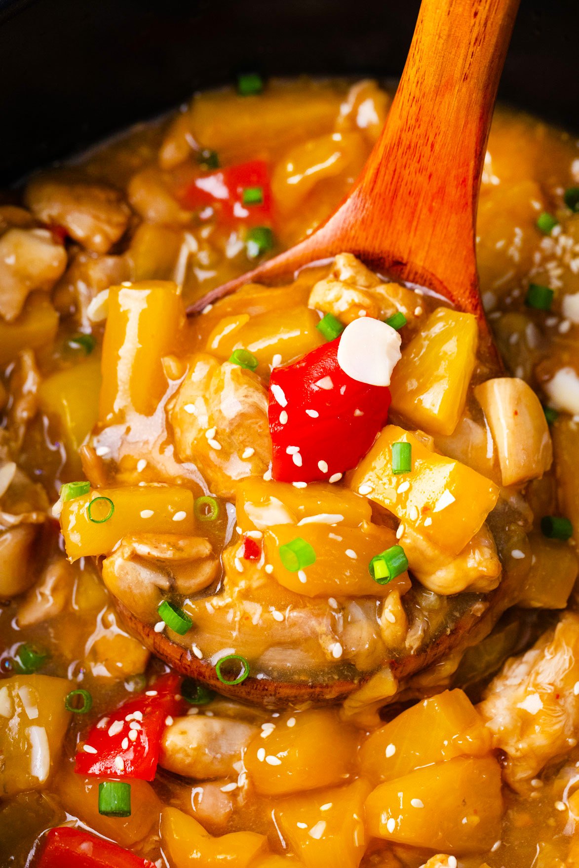 A ladle of slow cooker Hawaiian chicken with bell peppers and pineapple pieces.