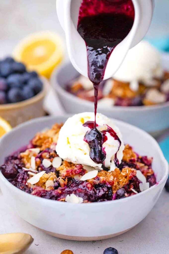 pouring blueberry sauce over ice cream on top of blueberry crisp