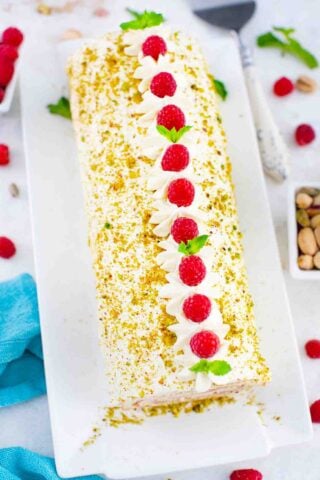 overhead shot of pistachio raspberry swiss roll on a white plate