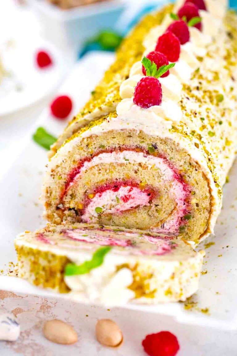 pistachio raspberry swiss roll garnished with whipped cream and fresh raspberries