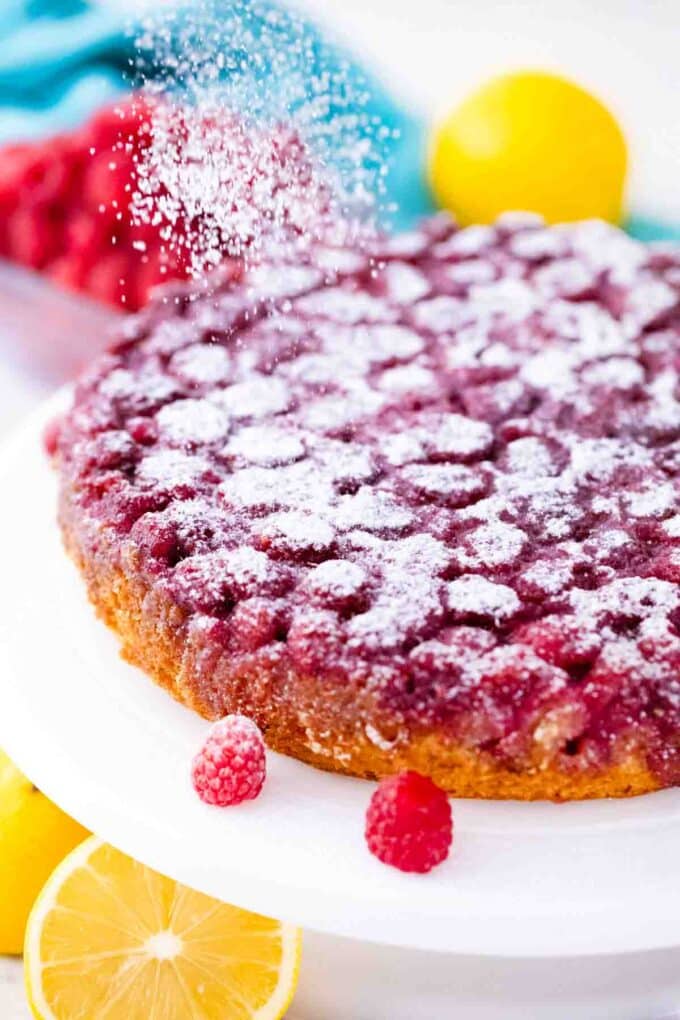 sprinkling powdered sugar on top of raspberry upside down cake