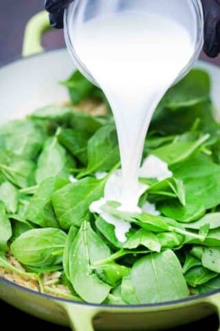 adding cream to spinach in a skillet