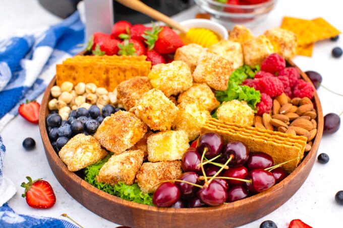 air fried brie on a wooden platter with cherries berries crackers and nuts