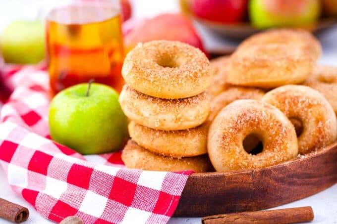 stalked apple cider donuts on a wooden tray with a green apple and apple cider in the background