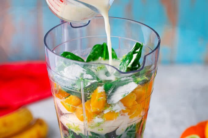 Adding spinach smoothie ingredients to a blender.