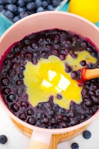 adding butter to blueberry pie filling in a saucepan