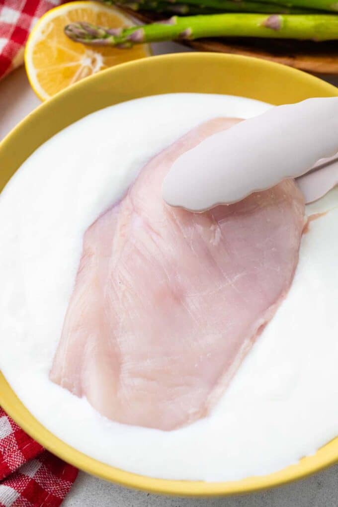 Dipping a chicken breast in a bowl of buttermilk.