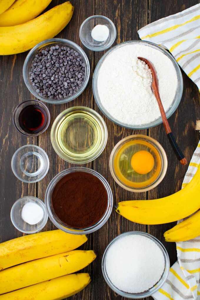 Overhead shot of chocolate banana bread muffins ingredients in bowls on a wooden surface.