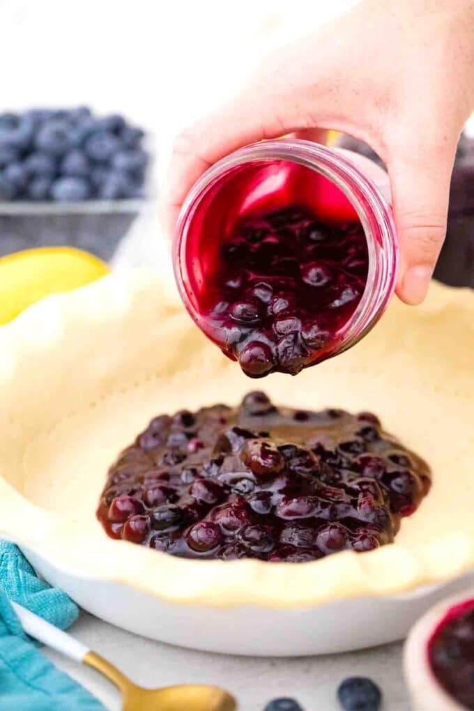 pouring blueberry pie filling from a mason jar into a pie crust
