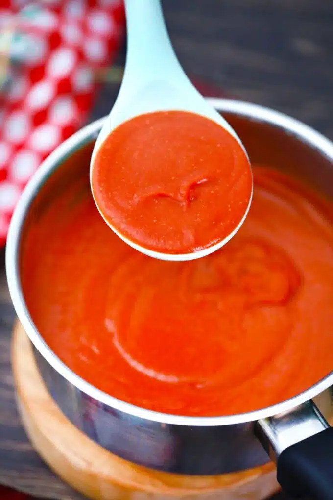 a spoonful of enchilada sauce over a saucepan with the sauce