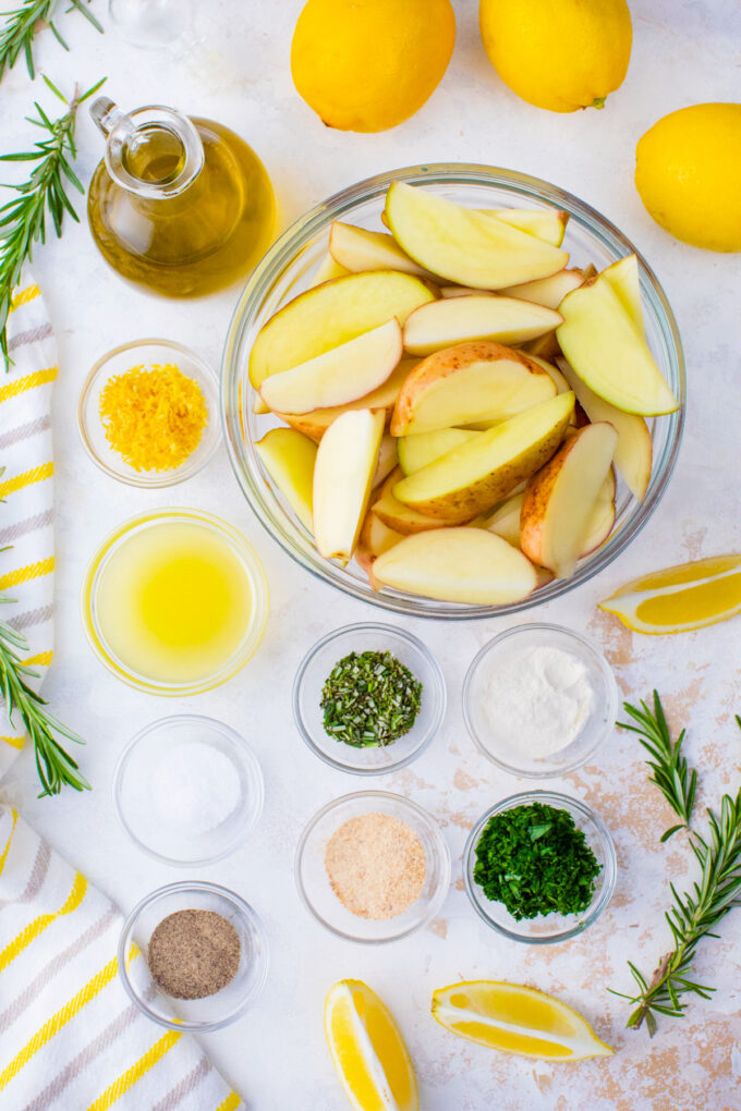 Overhead shot of grilled potatoes ingredients in bowls on a white surface.