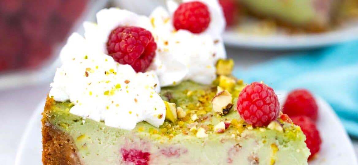 a slice of raspberry pistachio cheesecake with whipped cream and fresh raspberries