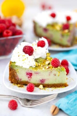 a slice of raspberry pistachio cheesecake with whipped cream and fresh raspberries