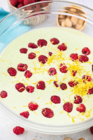 adding fresh raspberries and lemon zest to a bowl of green pistachio cheesecake filling