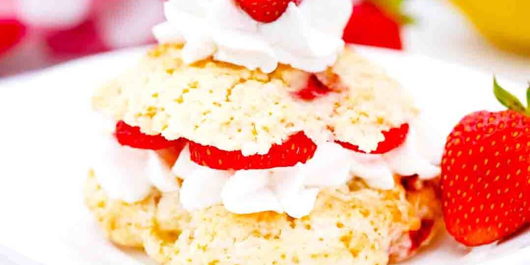 strawberry shortcakes on a white plate topped with whipped cream and fresh strawberries