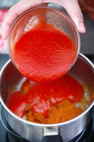 adding tomato sauce to a saucepan with chili powder and flour mix