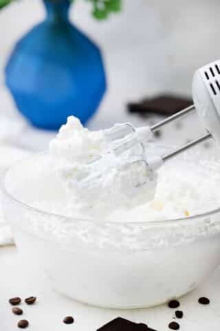 the whisk of a hand mixer covered in whipped cream on top of a bowl with whipped cream