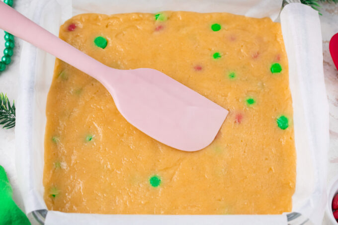 Pressing M&M cookie bars dough into a baking pan.