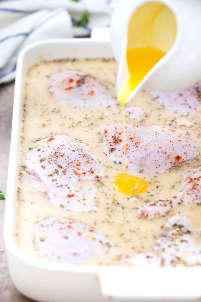 pouring butter onto chicken and rice in a casserole