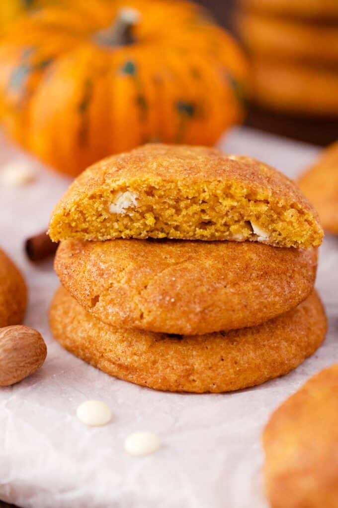 a pumpkin snickerdoodle cookie sliced in half revealing white chocolate chips inside, sits on two pumpkin snickerdoodle cookies