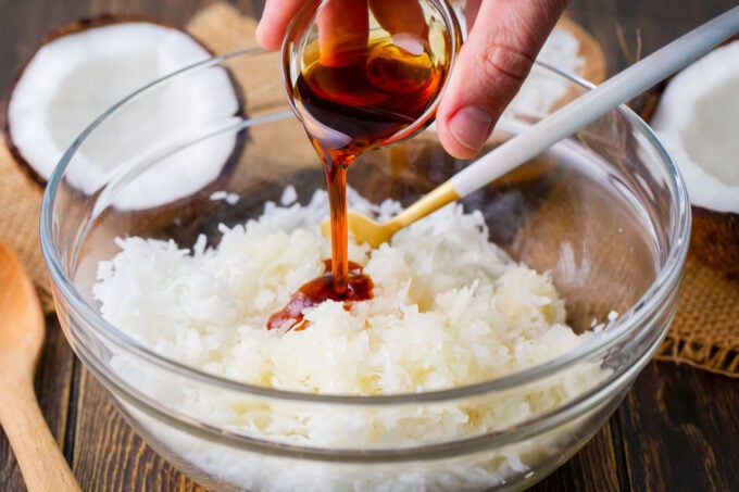 Adding maple syrup to shredded coconut in a bowl.