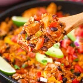 serving cheesy fiesta chicken from a skillet using a wooden spoon