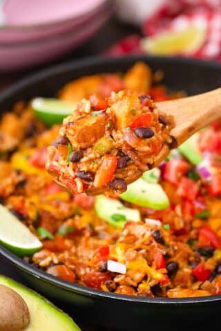 serving cheesy fiesta chicken from a skillet using a wooden spoon