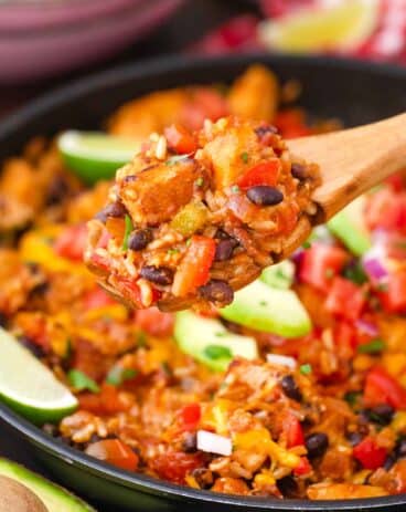 serving cheesy fiesta chicken from a skillet using a wooden spoon
