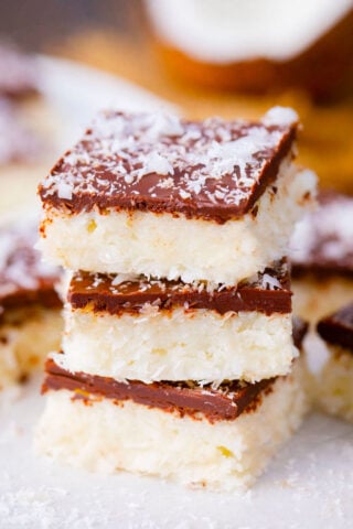 Stacked coconut crack bars topped with chocolate and shredded coconut flakes.