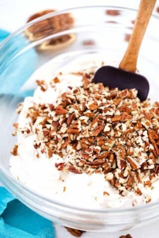 adding pecans to a bowl with a white creamy filling