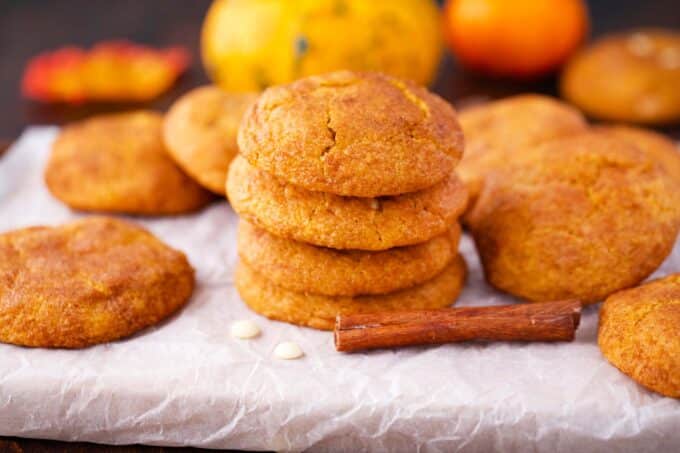 a stack of four pumpkin snickerdoodle cookies with more cookies around them on a cutting board covered with parchment paper