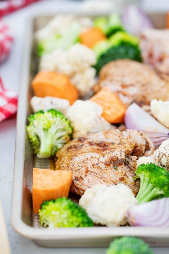 raw veggies and chicken thighs on a baking sheet