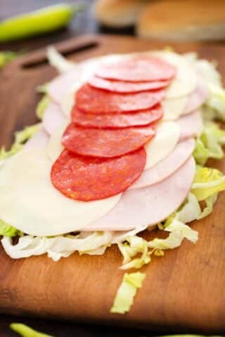 layers of chopped lettuce cold cuts and cheese slices on a cutting board