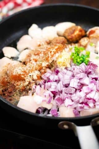 a skillet with chopped chicken breast spiced and diced red onion