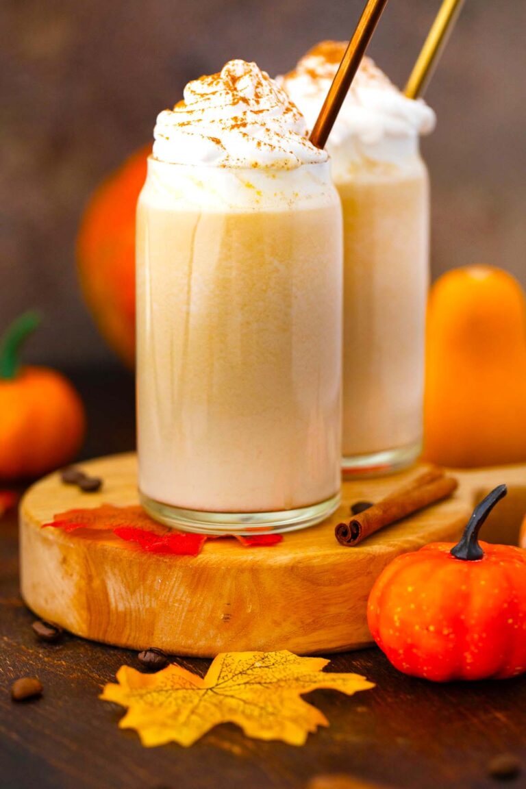 two homemade starbucks pumpkin spice latte with a tiny pumpkin and fall leaves next to them