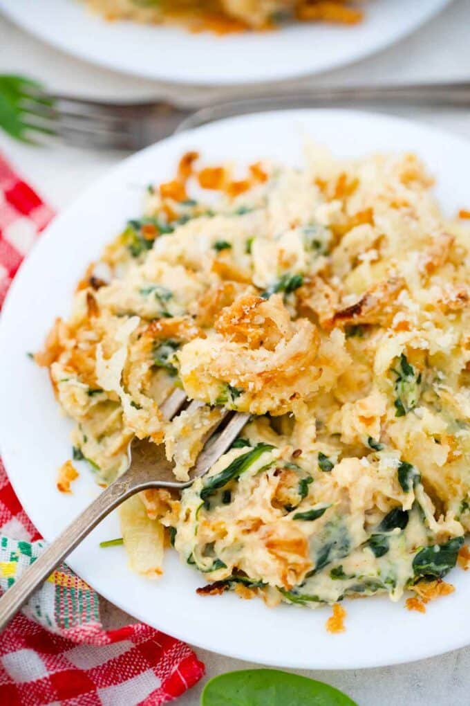 a plate with a hefty serving of cheesy spinach casserole with a fork in it