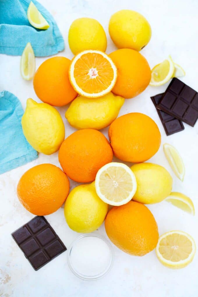 overhead shot of a pile of oranges and lemons sugar in a bowl and chocolate squares on a table