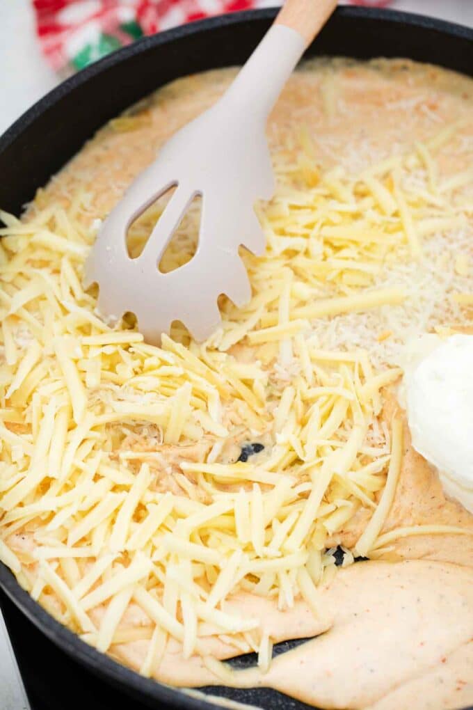 staring shredded cheese into a sauce in a skillet