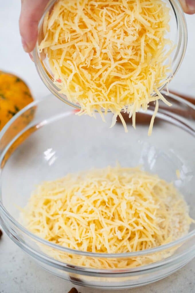 adding cheese from a small bowl to a large bowl