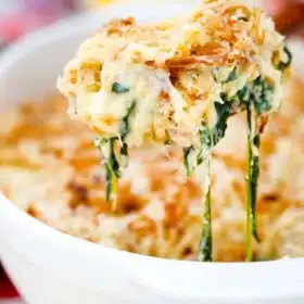 a large wooden spoon with a portion of spinach casserole on top of a casserole dish