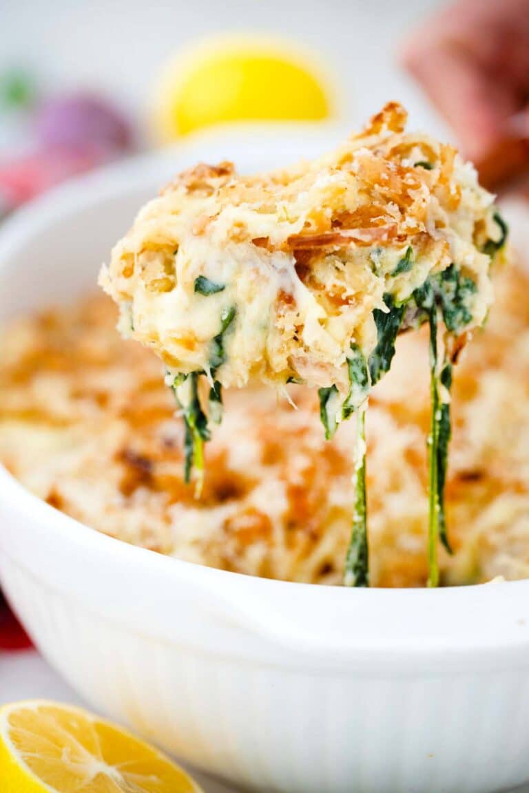 a large wooden spoon with a portion of spinach casserole on top of a casserole dish