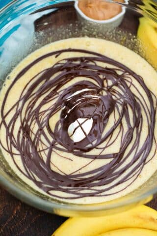 adding a swirl of melted chocolate to creamy banana bread batter