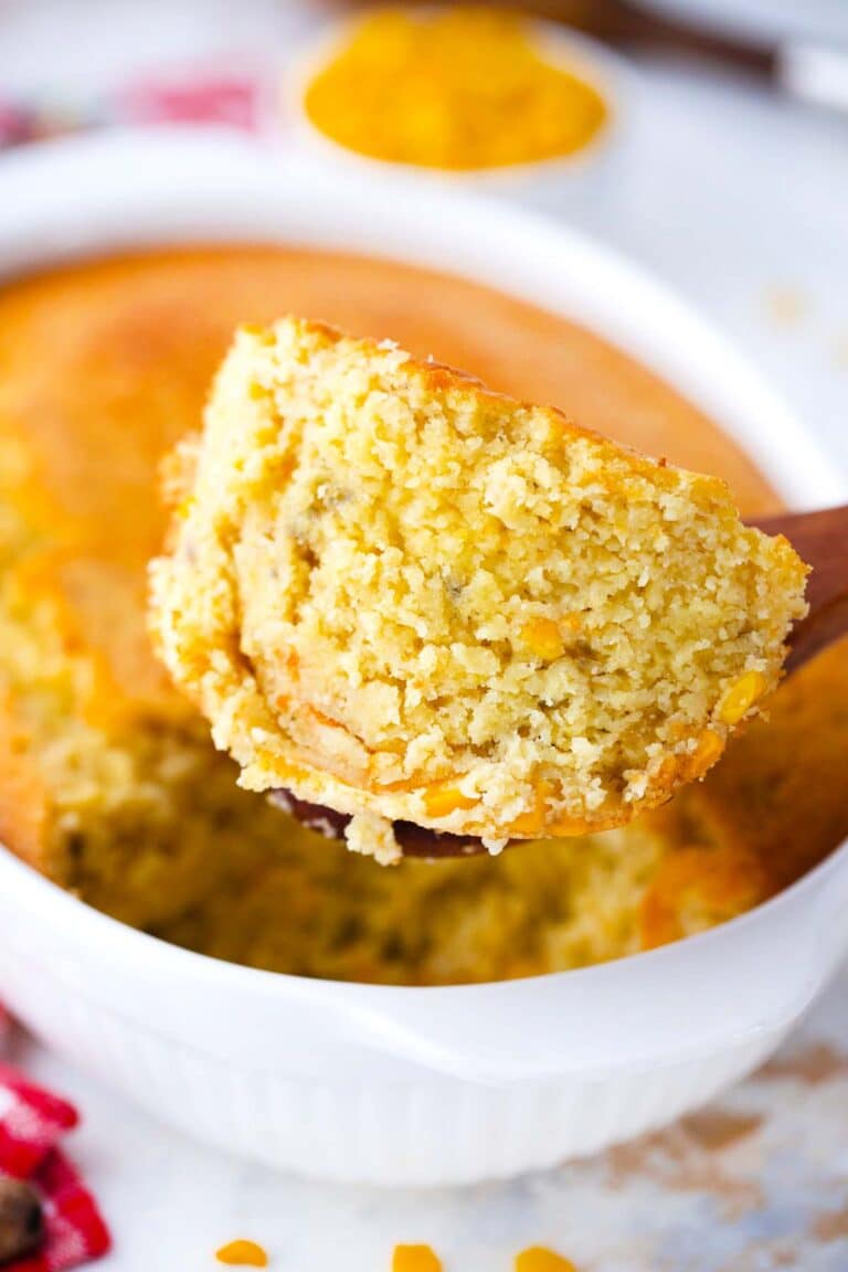 a large wooden spoon holding a hefty amount of corn pudding casserole with the casserole in the background