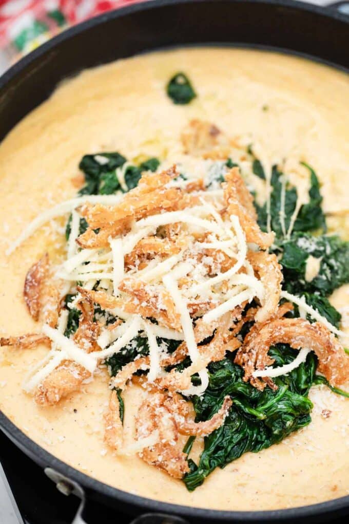 adding cooked spinach cheese and fried onions to a sauce in a skillet