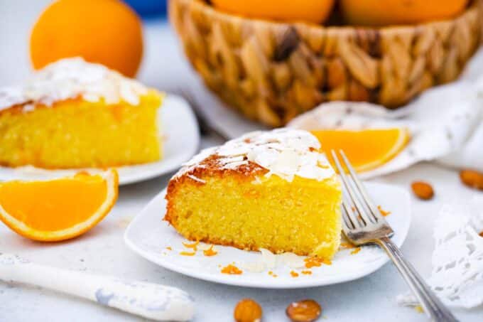 slices of almond orange cake topped with orange zest and a bowl with oranges in the background