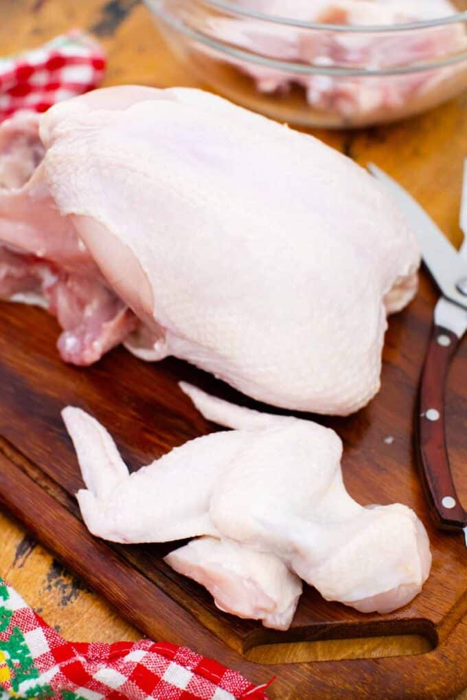 showing how to cut a whole chicken by cutting the legs and wings first with a kitchen scissor