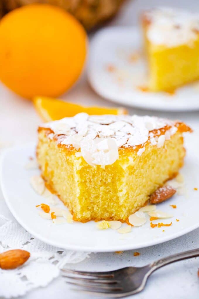 frontal shot of a slice of italian almond orange cake with another slice in the background and an orange
